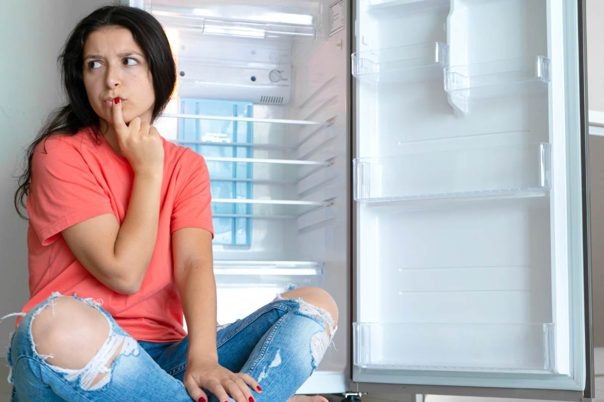 donna dubbiosa accanto a frigorifero aperto
