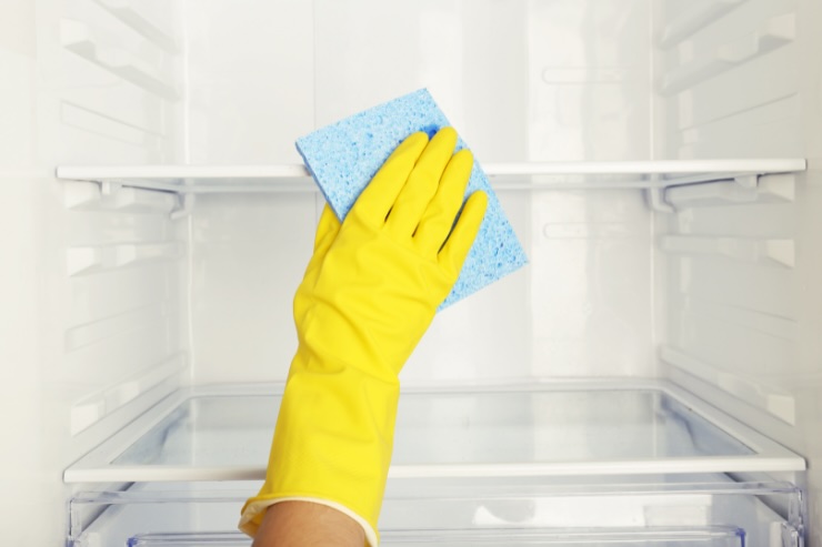 mano con guanto giallo che pulisce frigo con panno azzurro