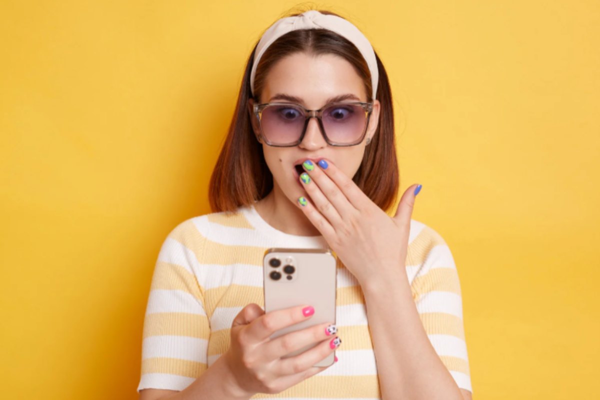 donna scioccata con una mano sulla bocca e nell'altra mano il cellulare
