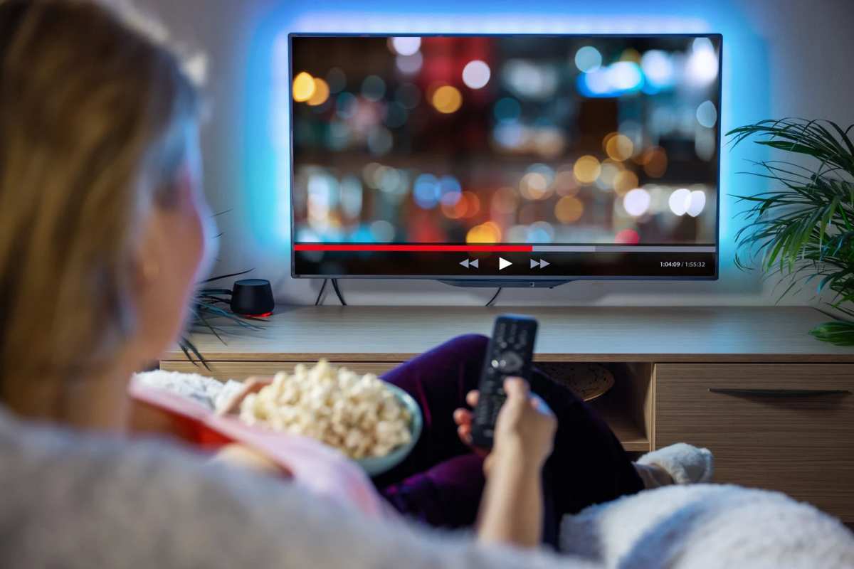 Donna con telecomando in mano e popcorn di fronte alla TV